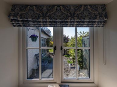 A window with patterned blinds overlooking a garden path with a hanging flower pot a bench and a shed at Bank Foot in Ambleside