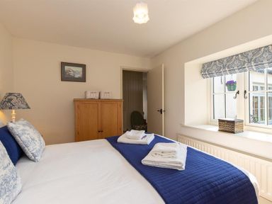A bedroom with a bed with blue and white bedding a wooden cabinet and a window with patterned blinds at Bank Foot in Ambleside