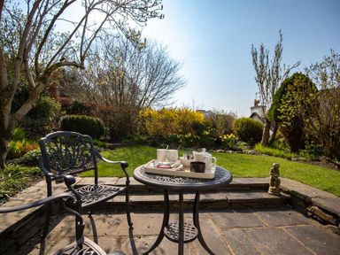 A patio with metal chairs and table set with teapot and cups overlooking a garden at Bank Foot in Ambleside