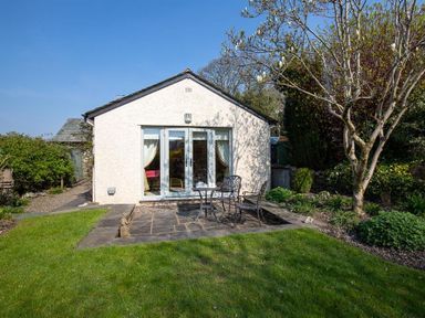 A garden patio with a table and two chairs in front of a detached white building at Bank Foot in Ambleside