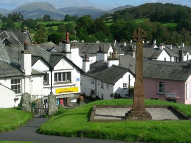 A stone cross monument on grass with white buildings and hills in the background at Jane's Cottage in Hawkshead
