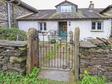 The front view of a stone cottage with a green door behind a black iron gate and stone wall at Janes Cottage in Hawkshead