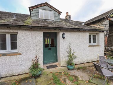 An exterior view of a cottage with a green door two windows two potted plants and outdoor chairs and table at Janes Cottage in Hawkshead