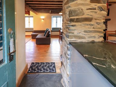 An open doorway showing a living room with a brown couch wooden floor stone wall and a countertop at Janes Cottage in Hawkshead