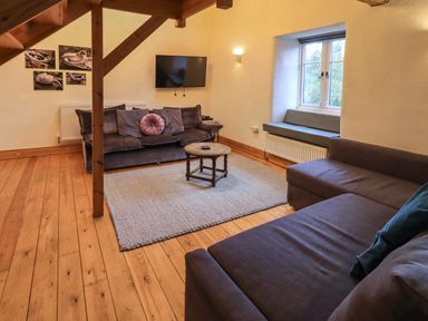 A sitting room with two sofas a round wooden coffee table a wall mounted television and a window seat at Janes Cottage in Hawkshead
