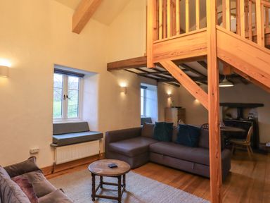 A living room with gray sofas a wooden round table and a wooden staircase at Janes Cottage in Hawkshead