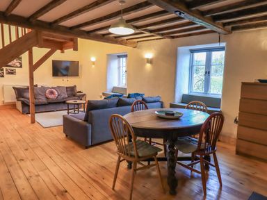 A living room with two sofas a round wooden dining table with chairs wooden floor and beams on the ceiling at Janes Cottage in Hawkshead