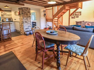 A dining area with wooden table and chairs next to a kitchen and living room with couch and staircase at Janes Cottage Hawkshead
