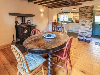 A dining area with a wooden table and chairs next to a stove and an open kitchen at Janes Cottage in Hawkshead