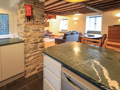 An open plan kitchen and living area with a stone pillar wooden beams a dining table with chairs and a seating area with sofas at Janes Cottage in Hawkshead