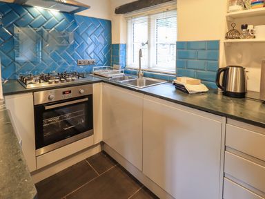 A kitchen with blue tiled backsplash a stainless steel stove oven sink kettle and countertop at Janes Cottage in Hawkshead