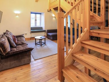A living room with two sofas a round coffee table a window seat and wooden stairs at Janes Cottage in Hawkshead