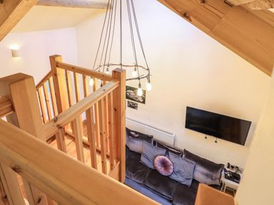 A living area with a sofa and cushions a wall-mounted television and a wooden staircase with a hanging light fixture at Janes Cottage in Hawkshead