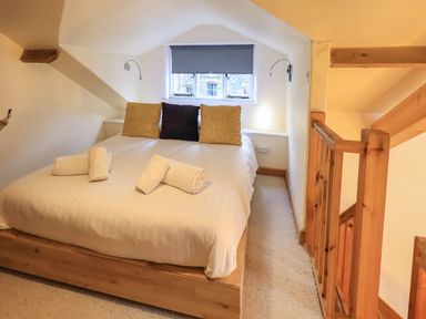 A bedroom with a bed with rolled towels and pillows near a window and wooden stairs at Janes Cottage in Hawkshead