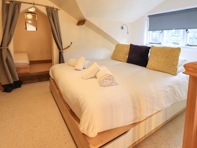 A bedroom with a large bed with folded towels and cushions next to a window and an alcove with a smaller bed at Janes Cottage in Hawkshead