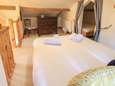 A bedroom with a bed with towels on it a wooden dresser a chair and a curtained sleeping area at Janes Cottage in Hawkshead