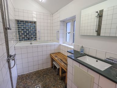 A bathroom with a bathtub shower handheld showerhead wooden bench window and sink at Janes Cottage in Hawkshead