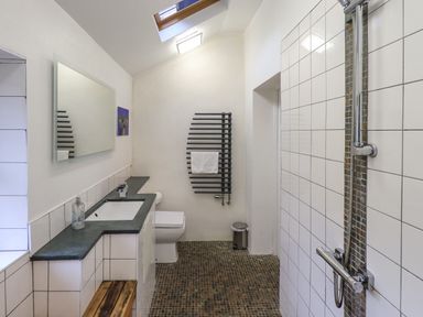 A bathroom with a tiled shower area a sink countertop a toilet a wall-mounted towel radiator and a skylight at Janes Cottage in Hawkshead