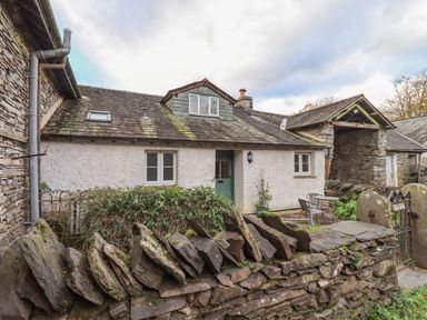 A stone cottage with a green door and slate roof surrounded by a stone wall at Janes Cottage in Hawkshead