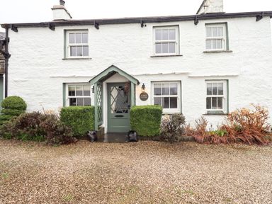 Front facade of a white cottage with green door and windows and bushes at Nurses Cottage Hawkshead