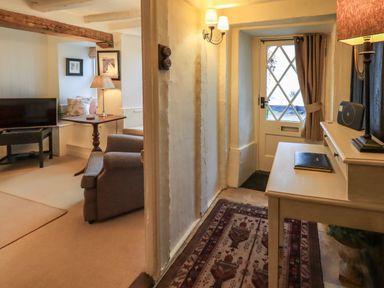 A hallway with a rug and table lamp next to a door and a living room with armchair television and side table at Nurses Cottage in Hawkshead