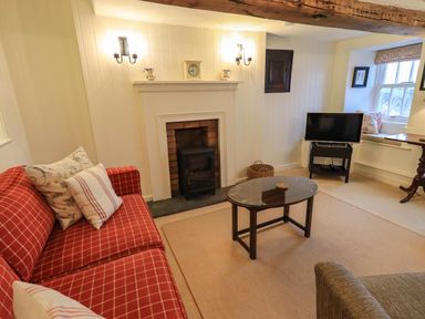 A living room with a red checkered sofa a glass coffee table a fireplace and a television at Nurses Cottage in Hawkshead