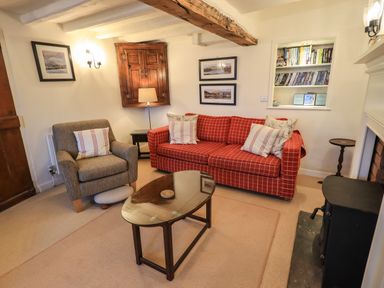 A living room with a red sofa and armchair a glass coffee table and a wood stove at Nurses Cottage in Hawkshead