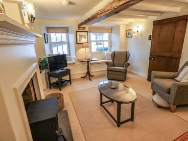 A sitting room with armchairs a coffee table a television wood stove and wooden door at Nurses Cottage in Hawkshead