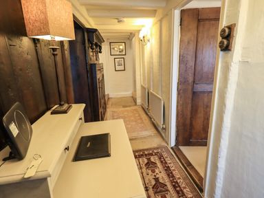 A hallway with a white desk, a lamp, rugs on the floor, wooden door, and framed pictures on the wall at Nurses Cottage in Hawkshead