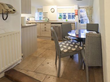 A kitchen area with a round dining table surrounded by four chairs and cabinets along the walls at Nurses Cottage in Hawkshead