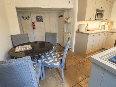 A kitchen with a round dining table and four chairs next to beige cabinets and countertop at Nurses Cottage in Hawkshead