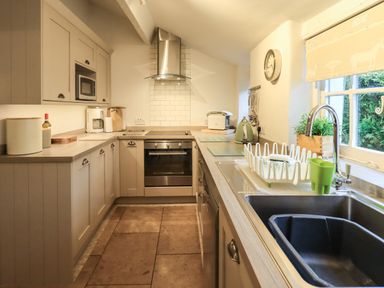 A kitchen with cabinets a sink an oven a range hood and a window at Nurses Cottage in Hawkshead