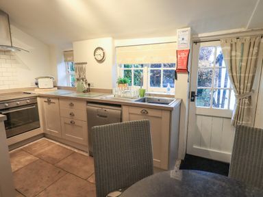 A kitchen with cabinets an oven a dishwasher a sink a door with windows and a round table with chairs at Nurses Cottage in Hawkshead