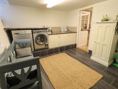 A laundry room with a washing machine dishwasher bench with pillow and a cabinet at Nurses Cottage in Hawkshead