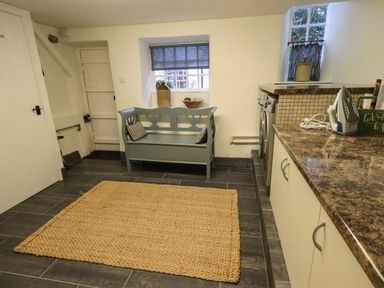 A utility room with a woven rug a bench under a window and a countertop with an iron at Nurses Cottage in Hawkshead