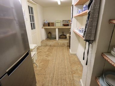 A kitchen pantry with stone flooring a rug shelves with cups and plates and a metal refrigerator at Nurses Cottage in Hawkshead