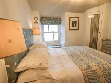 A bedroom with a bed framed by two lamps a window with a patterned blind and a bench below it at Nurses Cottage in Hawkshead