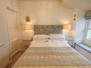 A bedroom with a double bed two bedside tables with lamps a window seat and a door at Nurses Cottage in Hawkshead