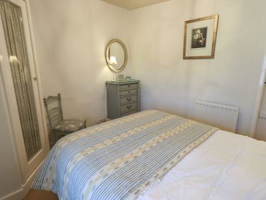 A bedroom with a bed a chair a chest of drawers a round mirror and a framed picture at Nurses Cottage in Hawkshead