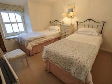 A bedroom with two single beds a small chest of drawers with lamps a window and a chair at Nurses Cottage in Hawkshead