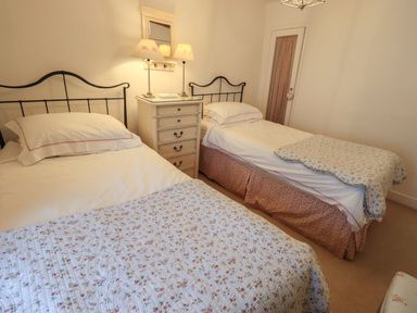 A bedroom with two single beds a white bedside table with two lamps and a wall mirror at Nurses Cottage in Hawkshead