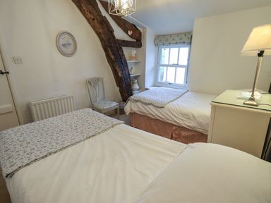 A bedroom with two single beds a wooden chair a window with floral blind and a bedside table with a lamp at Nurses Cottage in Hawkshead
