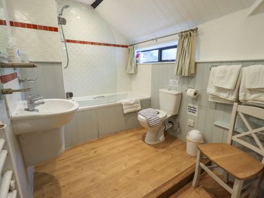 A bathroom with a bathtub shower sink toilet towels and a chair at Nurses Cottage in Hawkshead