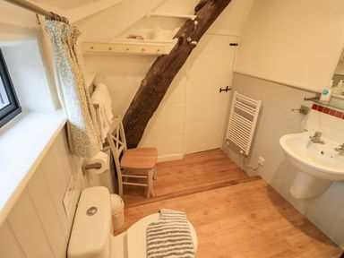 A bathroom with a toilet, wooden chair, sink, towel rack, and wooden beam at Nurses Cottage in Hawkshead