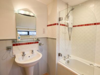 A bathroom with a pedestal sink and mirror and a bathtub with a showerhead and glass screen at Nurses Cottage in Hawkshead