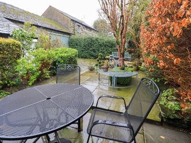 An outdoor patio with metal table and chairs next to plants and shrubs at Nurses Cottage in Hawkshead