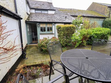 A patio with metal table and chairs outside a white cottage with shrubs at Nurses Cottage in Hawkshead