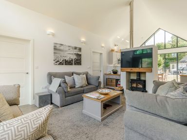 A living room with gray sofas a coffee table a wood stove and large windows at Wood Sage in Bamburgh