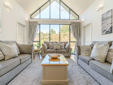 A living room with three sofas a coffee table and large windows at Wood Sage in Bamburgh