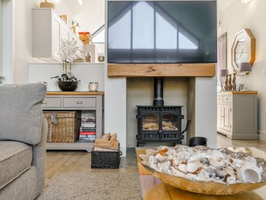 A living room with a wood burning stove TV on mantel wicker baskets and cabinets at Wood Sage in Bamburgh